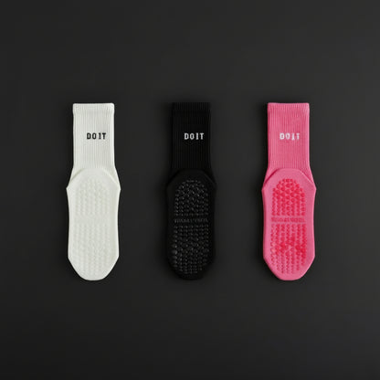 Three pairs of DOIT scrub socks in white, black, and rose red on a black studio b background
